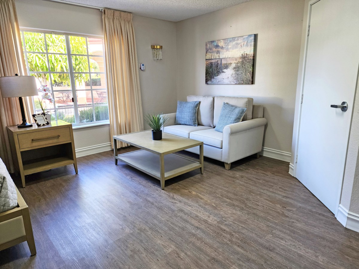 A cozy living room with a sofa, coffee table, and a large window letting in natural light.
