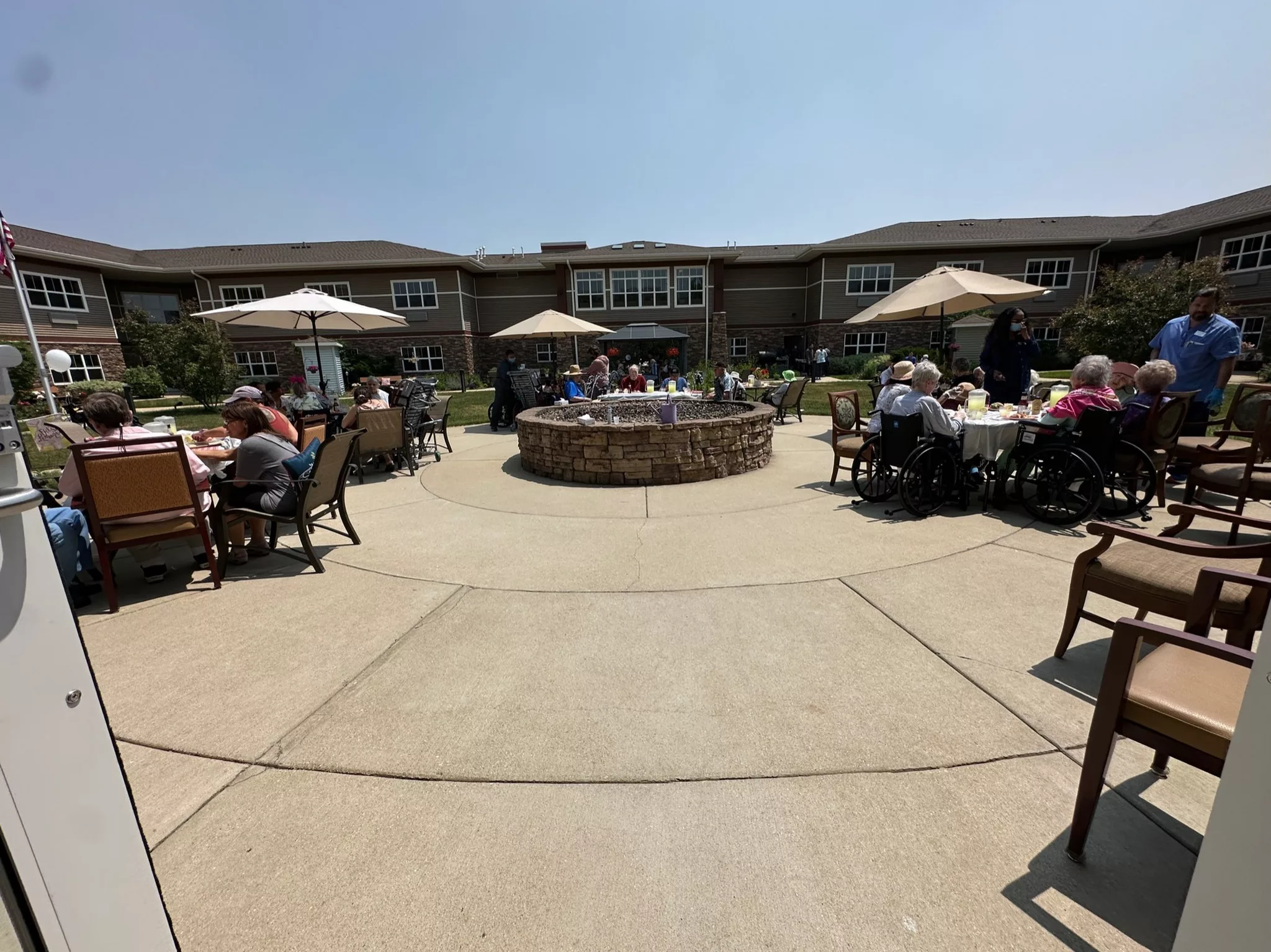 A sunny day on an outdoor patio filled with people enjoying a social gathering under umbrellas.