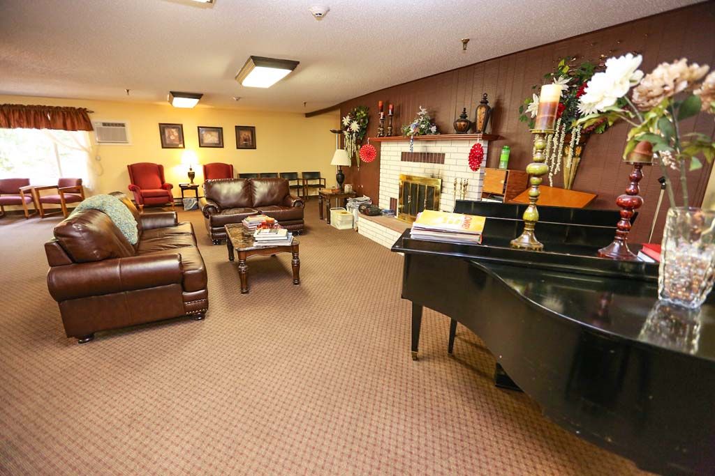 A cozy living room with a grand piano, comfortable seating, and a decorative fireplace.