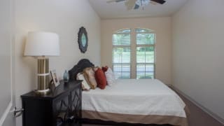 A cozy bedroom with a neatly made bed, decorative pillows, and large windows.