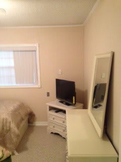 A simple bedroom featuring a TV, dresser with mirror, and a bed near a window.
