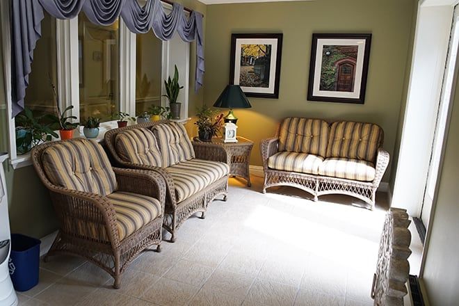 A cozy living room featuring wicker furniture with striped upholstery, complemented by a coffee table, lamp, and framed artwork on the walls.