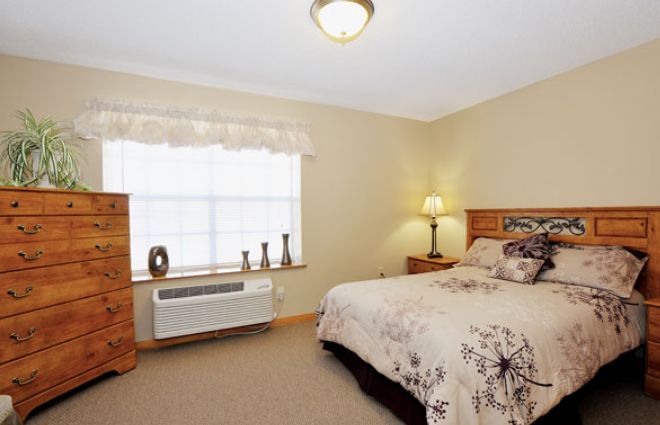A cozy bedroom with a double bed, side table, and lamp next to a large window.