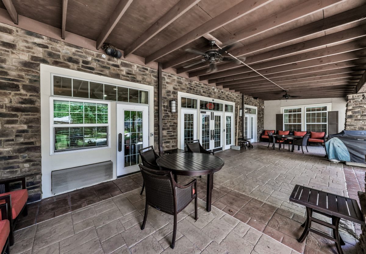 A spacious covered patio area with outdoor furniture, brick walls, and large glass doors.
