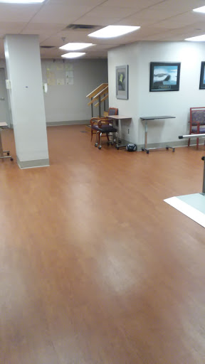 A view of a waiting area in a hospital with wooden flooring and some chairs and tables.