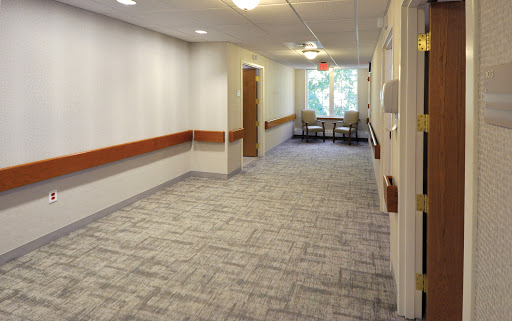 A well-lit hallway in a healthcare facility, featuring a comfortable waiting area with chairs.