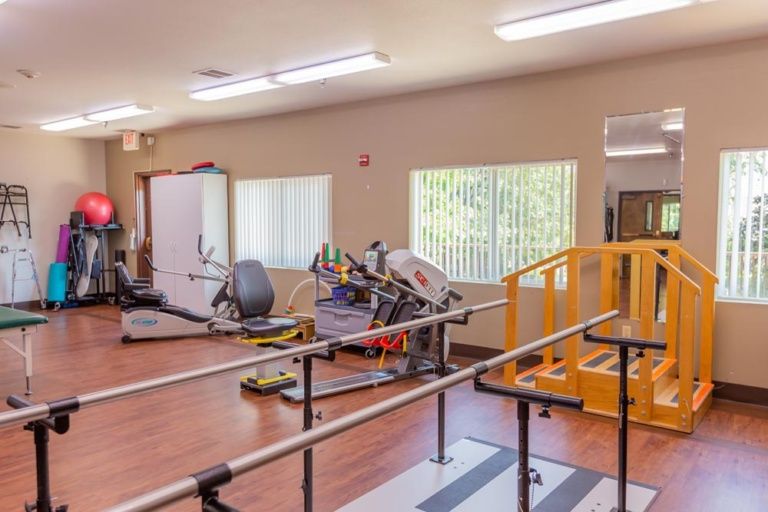 A rehabilitation therapy room equipped with exercise machines and parallel bars.