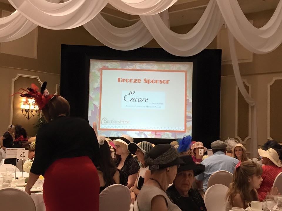 A formal event with a presentation screen displaying 'Present Sponsor' and people seated at banquet tables.