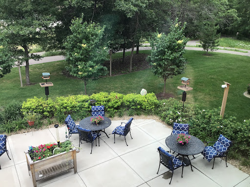 A serene outdoor patio setting with blue chairs and tables, surrounded by lush greenery.