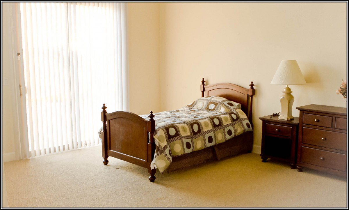 A minimalist bedroom with a single bed, nightstand, and lamp by a window.