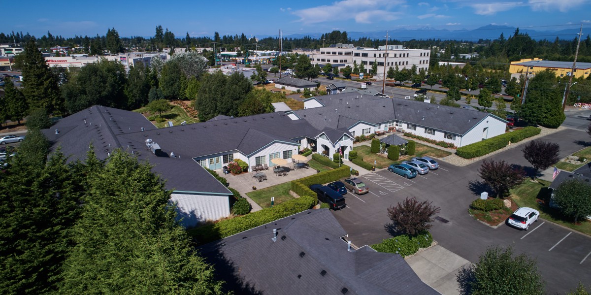 Aerial view of a suburban residential area with houses, trees, and a parking lot on a sunny day.