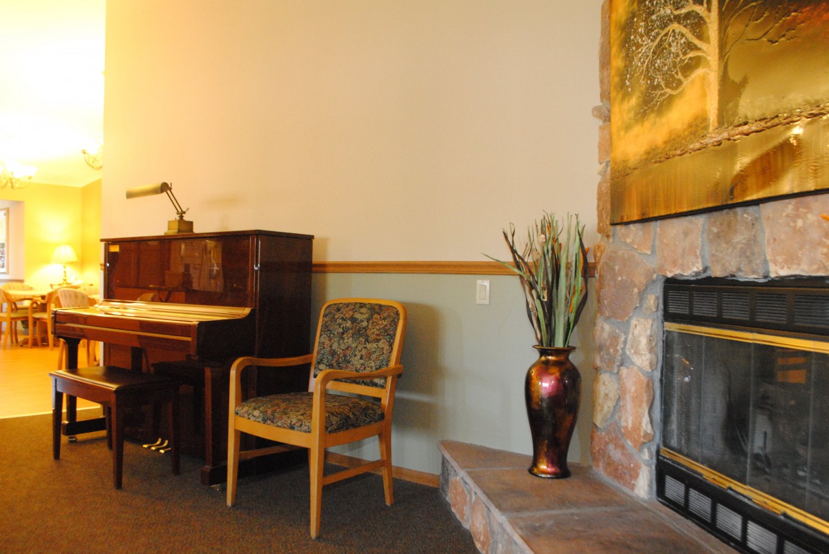 A cozy living room with a piano, chair, and fireplace adorned with a decorative vase.