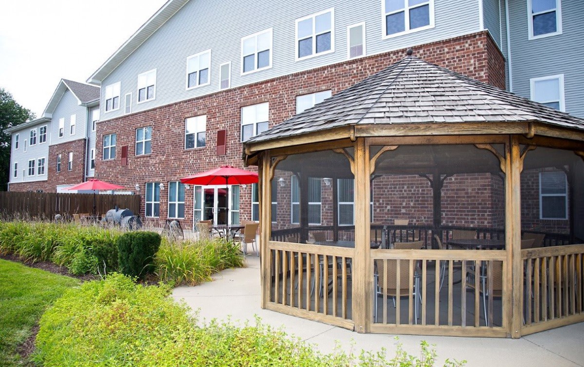 A well-maintained brick building with a wooden gazebo and outdoor seating area featuring red umbrellas.