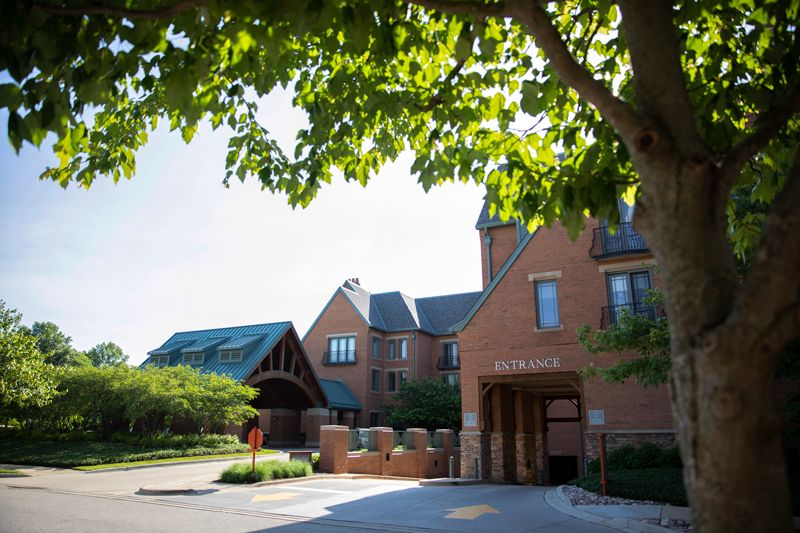 A sunny day outside a large brick building with trees and greenery.