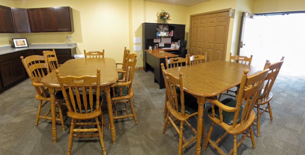 An office space with wooden tables and chairs, featuring a desk in the background.