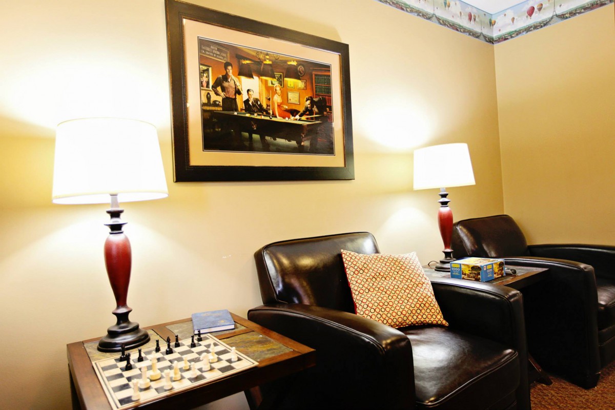 A cozy living room setup featuring armchairs, a chess board, and soft lighting from table lamps.