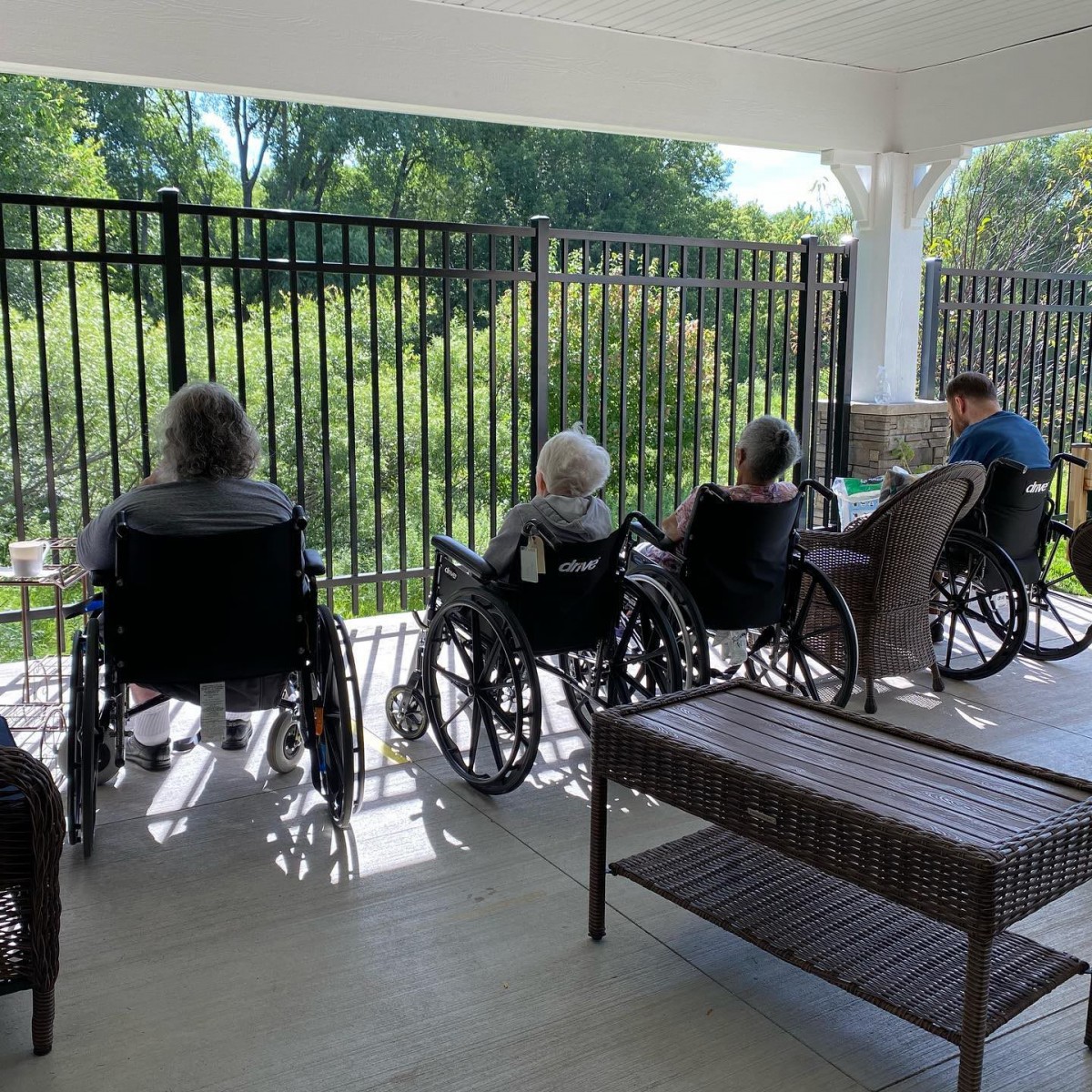 Elderly individuals in wheelchairs relaxing on a sunny patio.