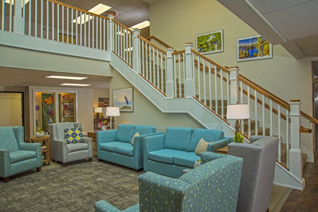 A cozy lobby area featuring teal sofas and a wooden staircase, adorned with modern lighting and artwork.