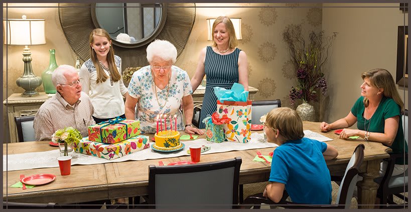 A family gathering to celebrate a birthday, featuring a cake and colorful presents.