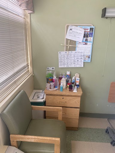 A small room corner featuring a wooden desk with various personal care products, a calendar, and wall decor.