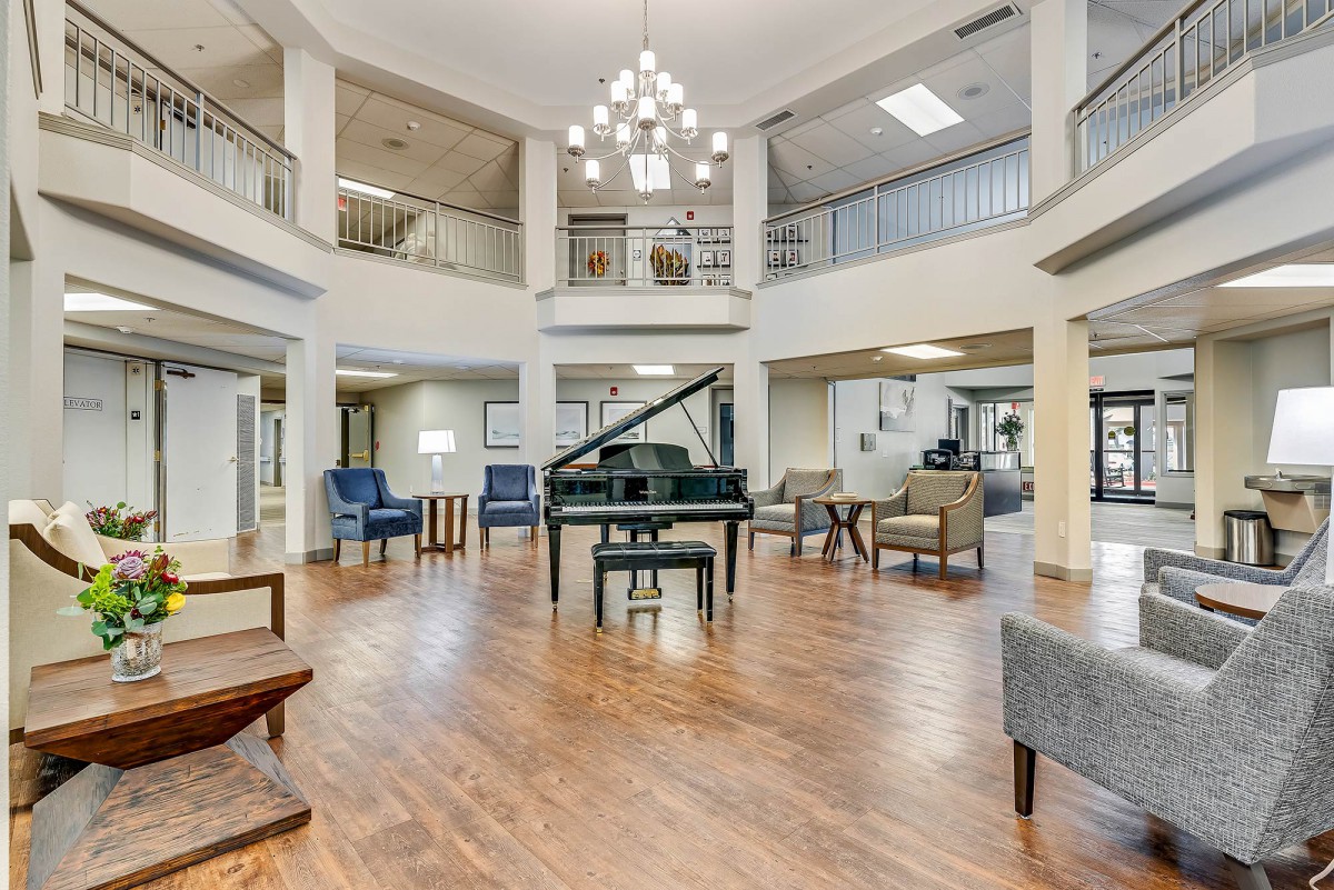 A spacious lobby area with a grand piano, comfortable seating, and a central chandelier.