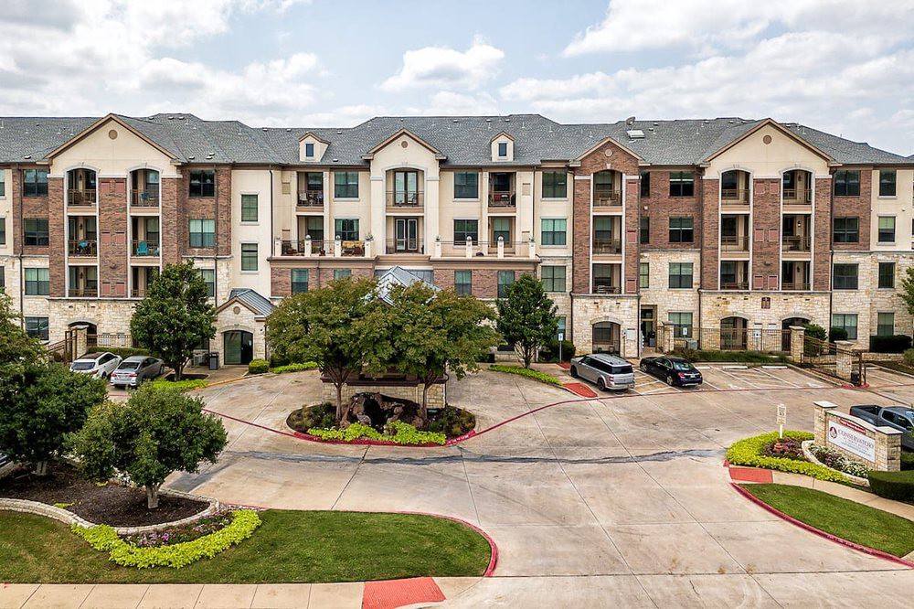 A modern apartment complex with a curved driveway and landscaped surroundings.
