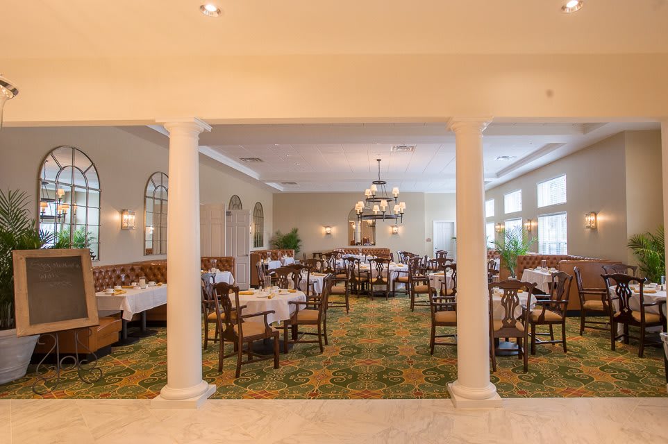 An elegant restaurant dining room with neatly arranged tables and chairs, featuring a chandelier and soft lighting.