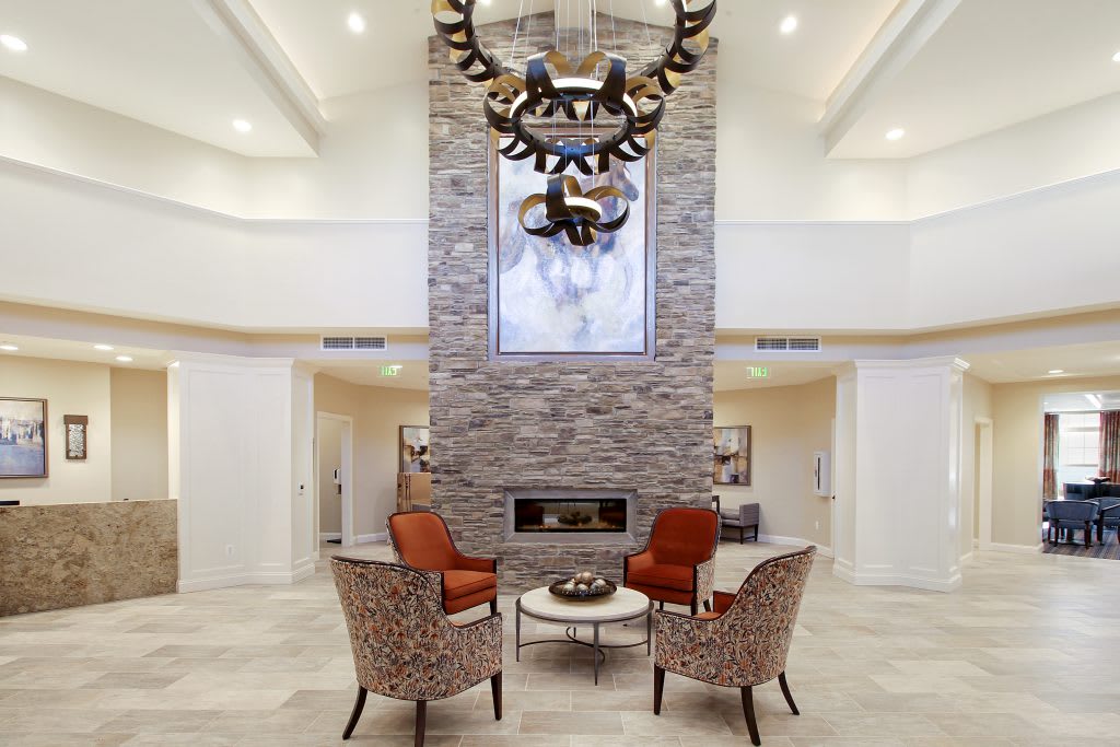 A modern living room features a central stone fireplace, elegant chandelier, and comfortable seating arrangement.
