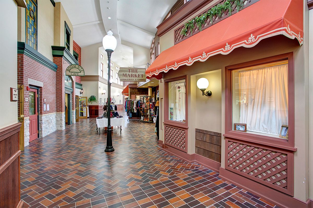 A quaint indoor shopping arcade with brick flooring, decorative storefronts, and vintage-style lampposts.