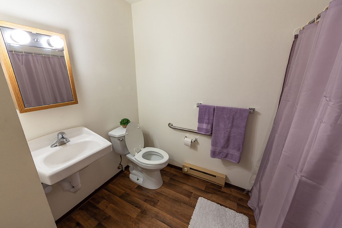A clean bathroom with a toilet, sink, mirror, towel, and shower curtain.