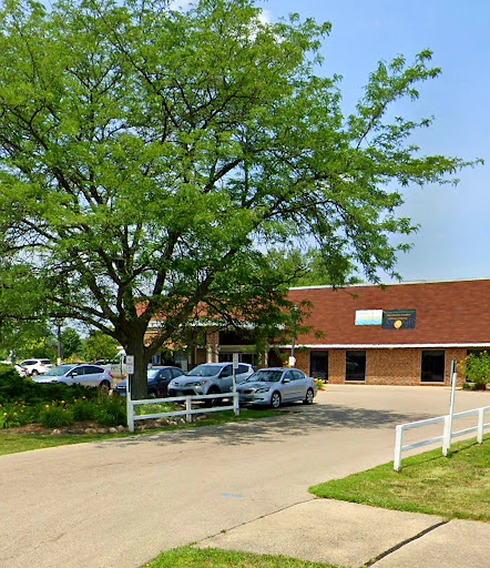 A view of a building surrounded by greenery and parked cars on a sunny day.