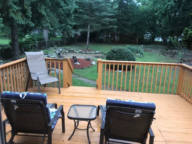 A cozy wooden deck with chairs and a table overlooking a lush backyard garden.