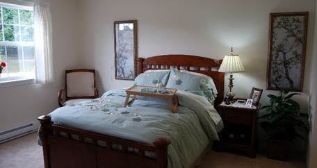 A cozy bedroom with a neatly made bed, a bedside table with a lamp, and soft lighting.