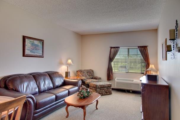 A cozy living room with a leather sofa, coffee table, and armchair under soft lighting.