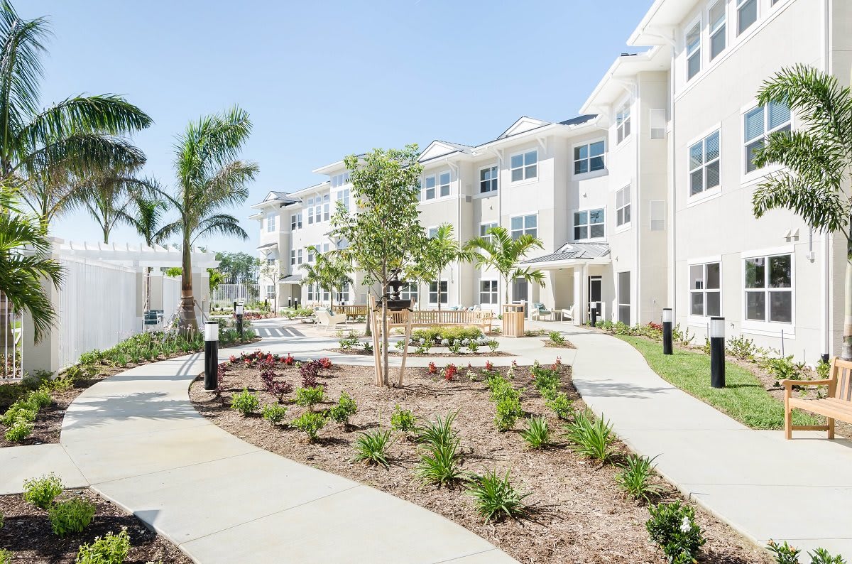 A modern apartment complex with well-maintained landscaping and palm trees under a clear blue sky.