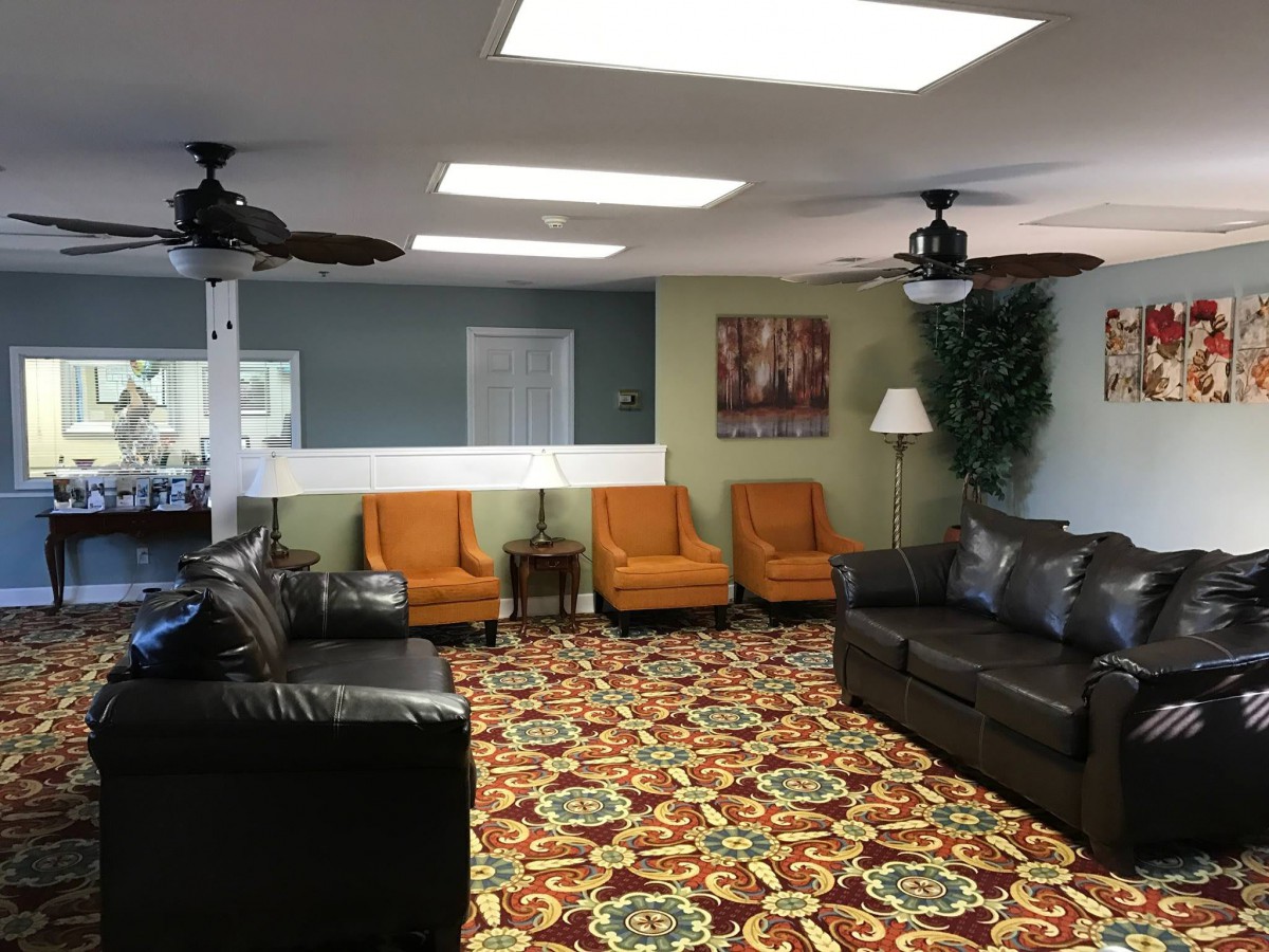 A cozy lobby with a mix of orange chairs and dark sofas, complemented by a colorful patterned carpet and ceiling fans.