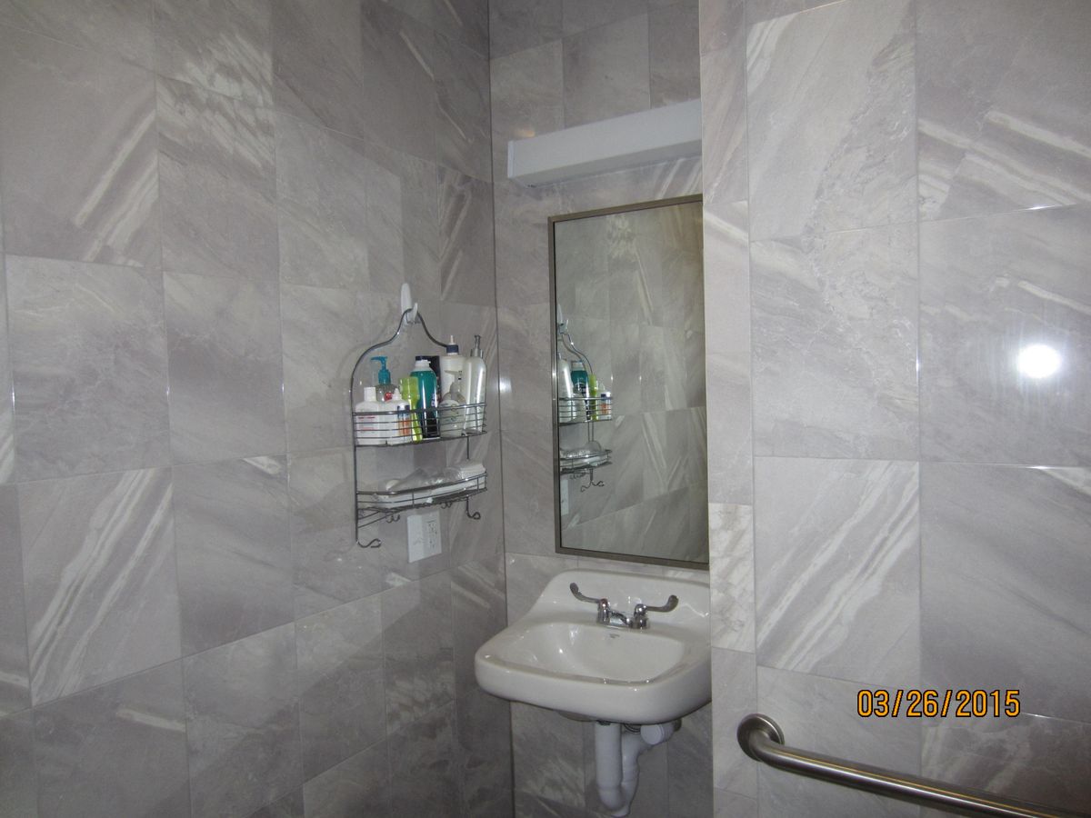 A small bathroom with tiled walls featuring a sink, mirror, and shelf with toiletries.