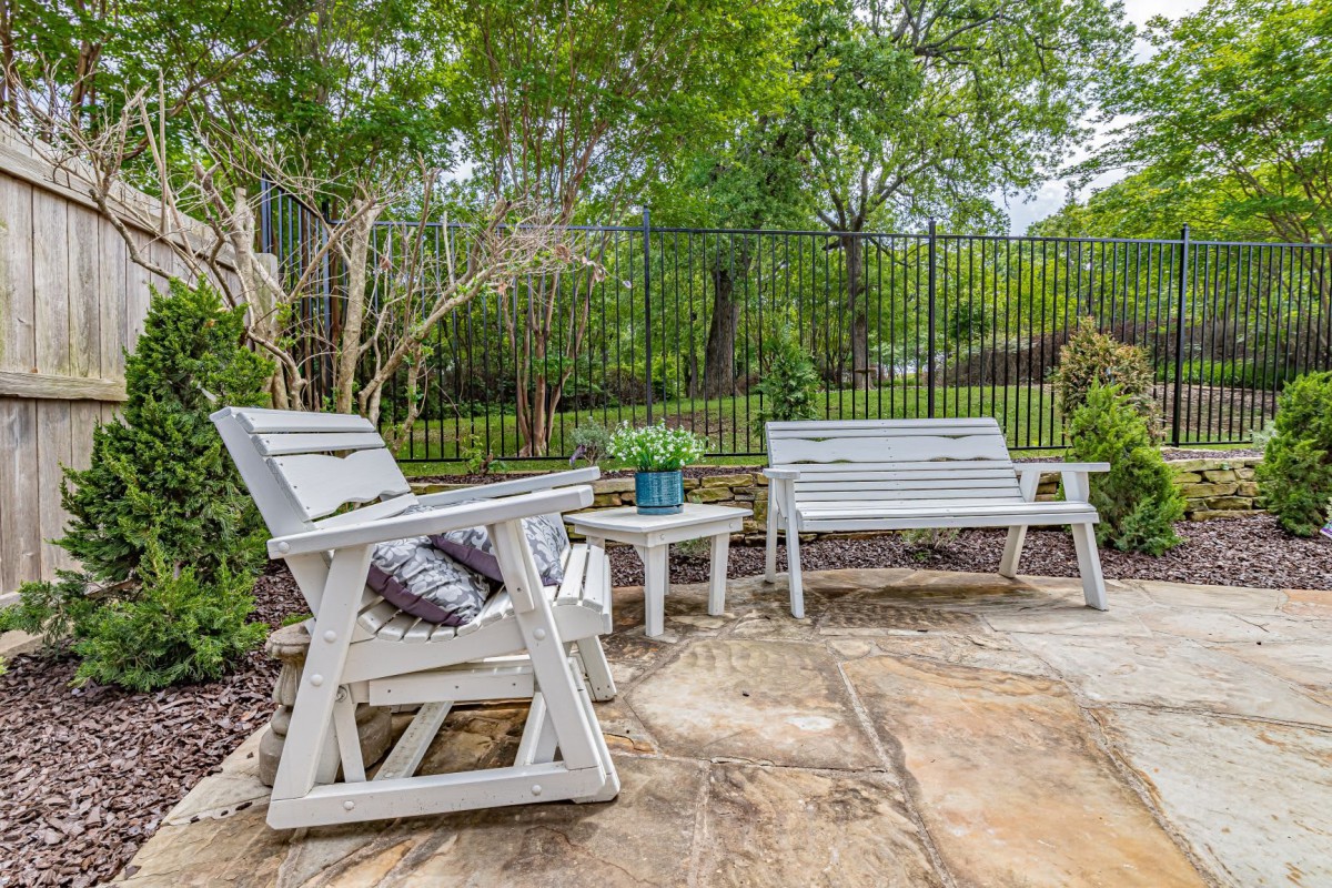 A cozy patio area with wooden furniture surrounded by a lush garden.