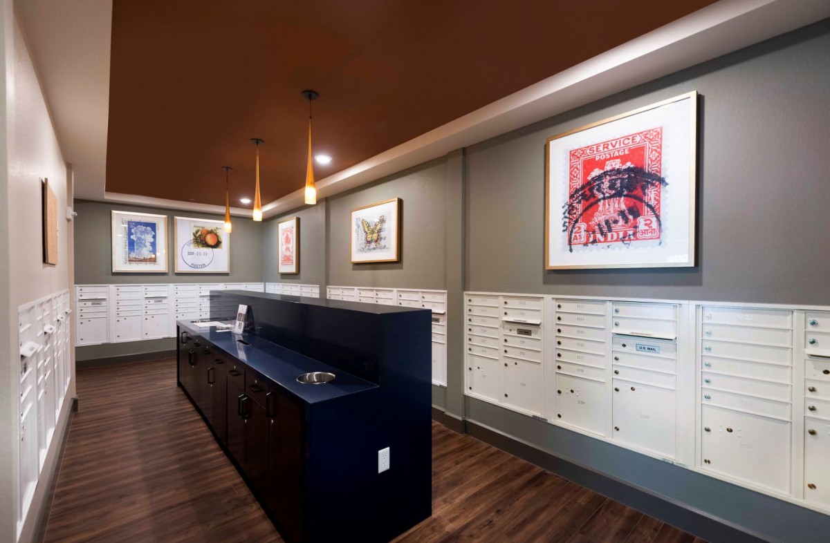 A modern mail room featuring sleek design with wall-mounted artwork and a row of white mailboxes.