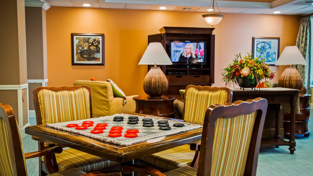 A cozy living room with a checkers game set up on a table, comfortable seating, and a television.