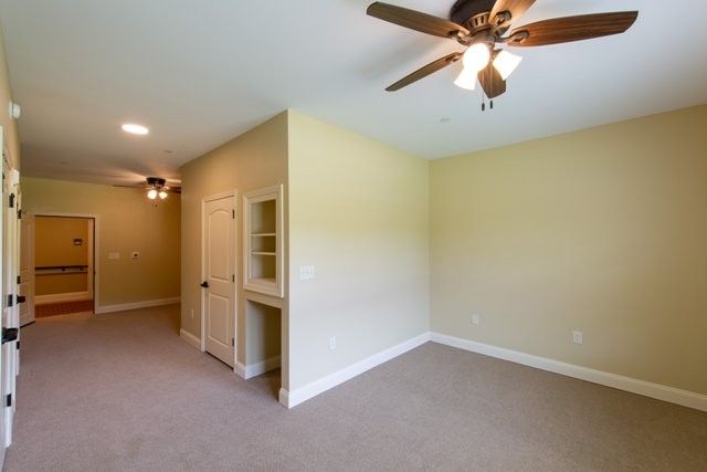 An empty room with beige walls, a ceiling fan, carpet flooring, and recessed lighting.