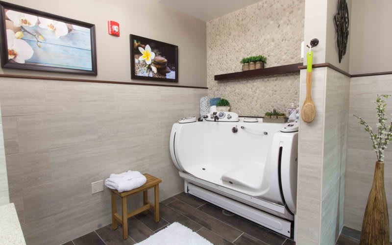 A modern bathroom featuring a spa-like bathtub with towels on a small wooden stool and decorative elements on the wall and shelf.