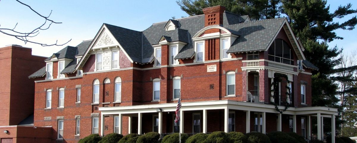 A large historic brick building featuring ornate architectural details and a wraparound porch.