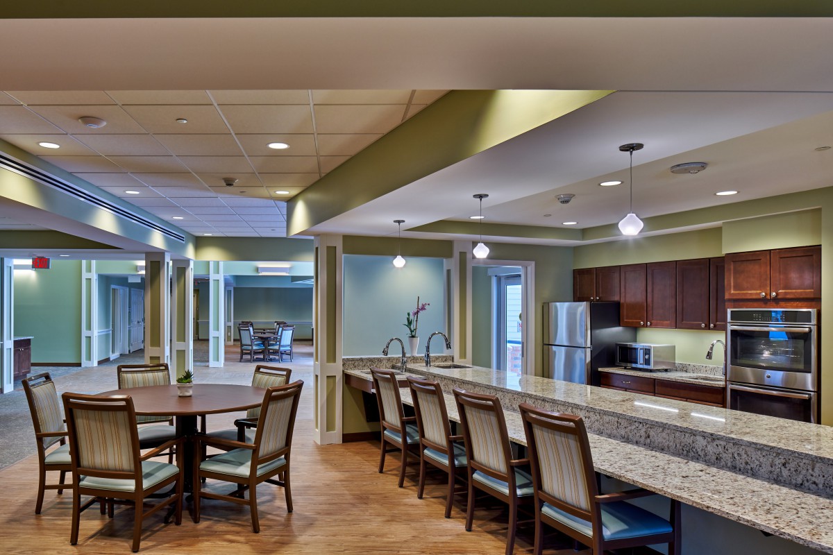 A modern kitchen and dining area featuring a long counter with bar stools, a circular dining table with chairs, and contemporary lighting fixtures.
