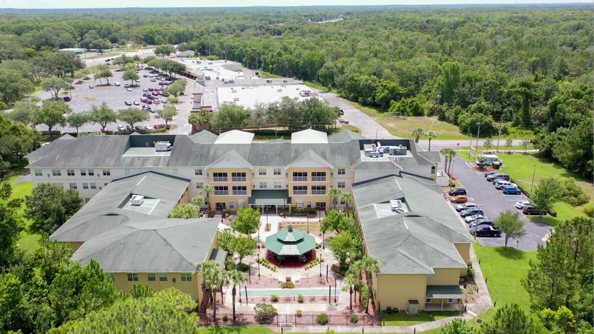 Aerial view of a large building complex surrounded by lush greenery and a parking lot.