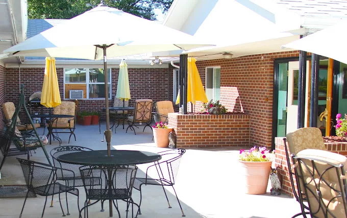 A sunny patio area with tables, chairs, and umbrellas outside a brick building.