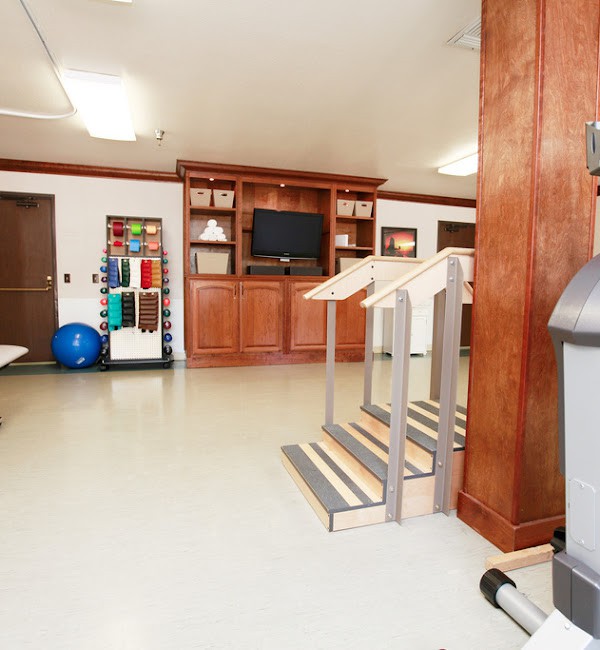 A spacious indoor gym area equipped with exercise equipment, stairs for rehabilitation, and a television.
