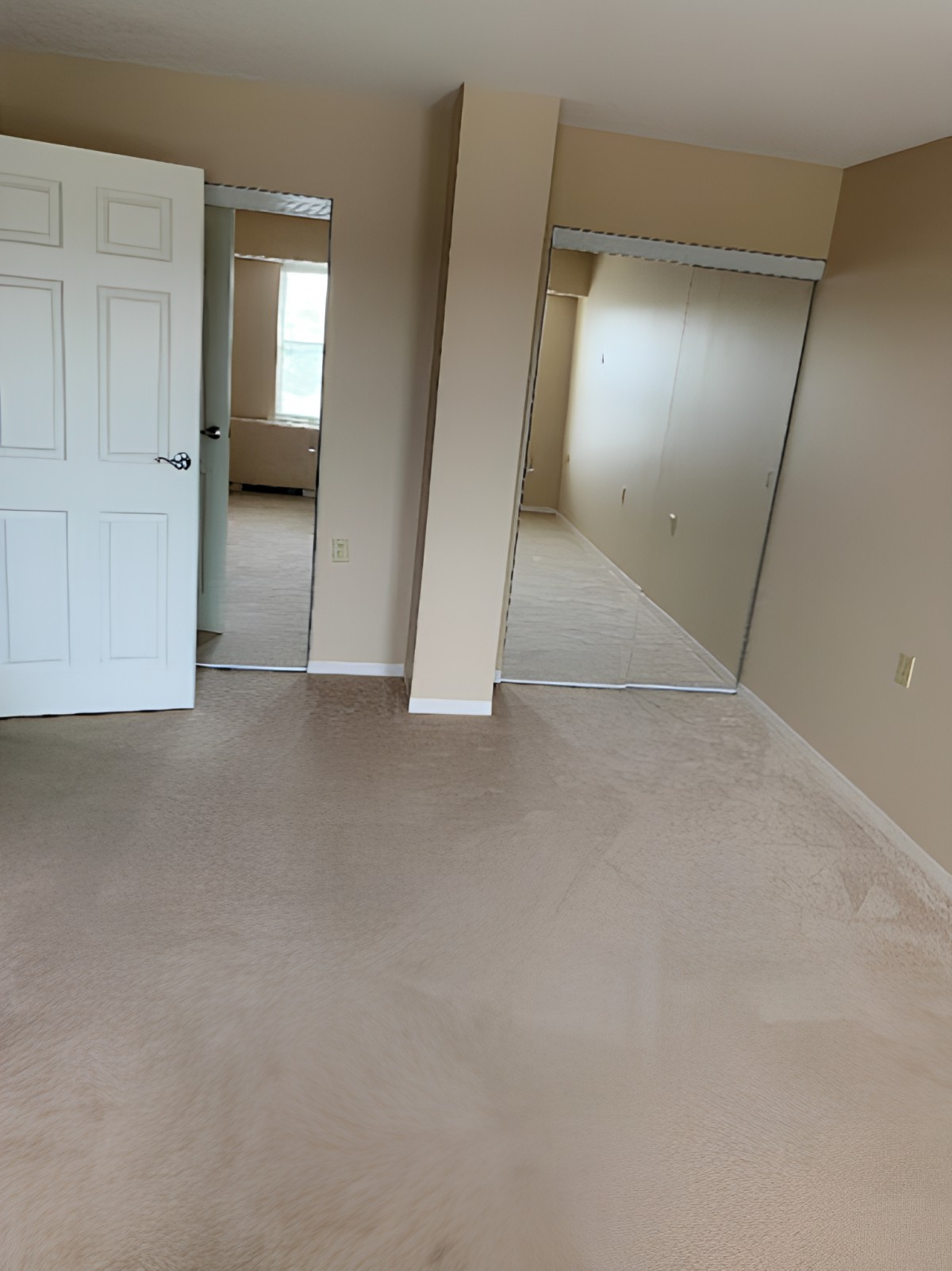 An empty bedroom with a carpeted floor and two closets.
