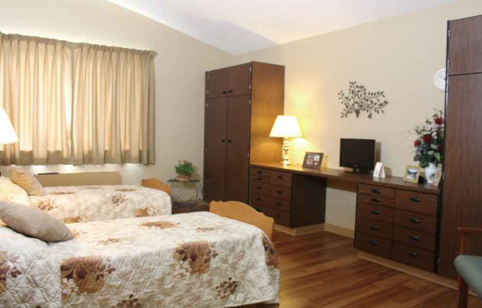 A cozy bedroom featuring twin beds, a desk with a lamp, and a wardrobe.