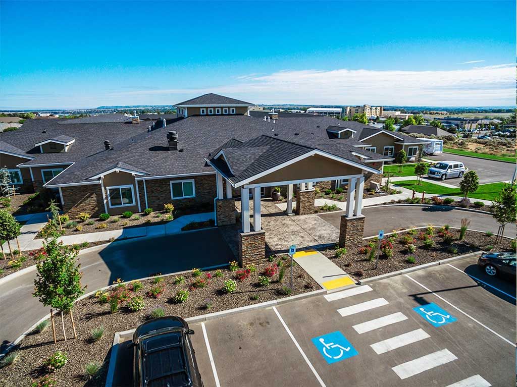 Aerial view of a building with a landscaped entrance and adjacent parking lot on a sunny day.